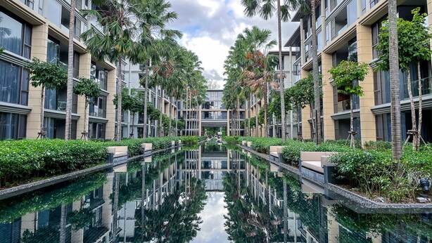Un hôtel moderne doté d’un bassin central aux eaux miroitantes, entouré de palmiers et de verdure.