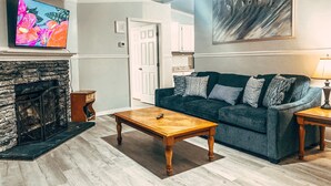 A living room with a stone fireplace, a dark blue sofa with patterned cushions, a wooden coffee table, and a flat-screen TV mounted above the fireplace. - Scenic Mountain Views 4 Bed 2 Bath (Cave Spring)