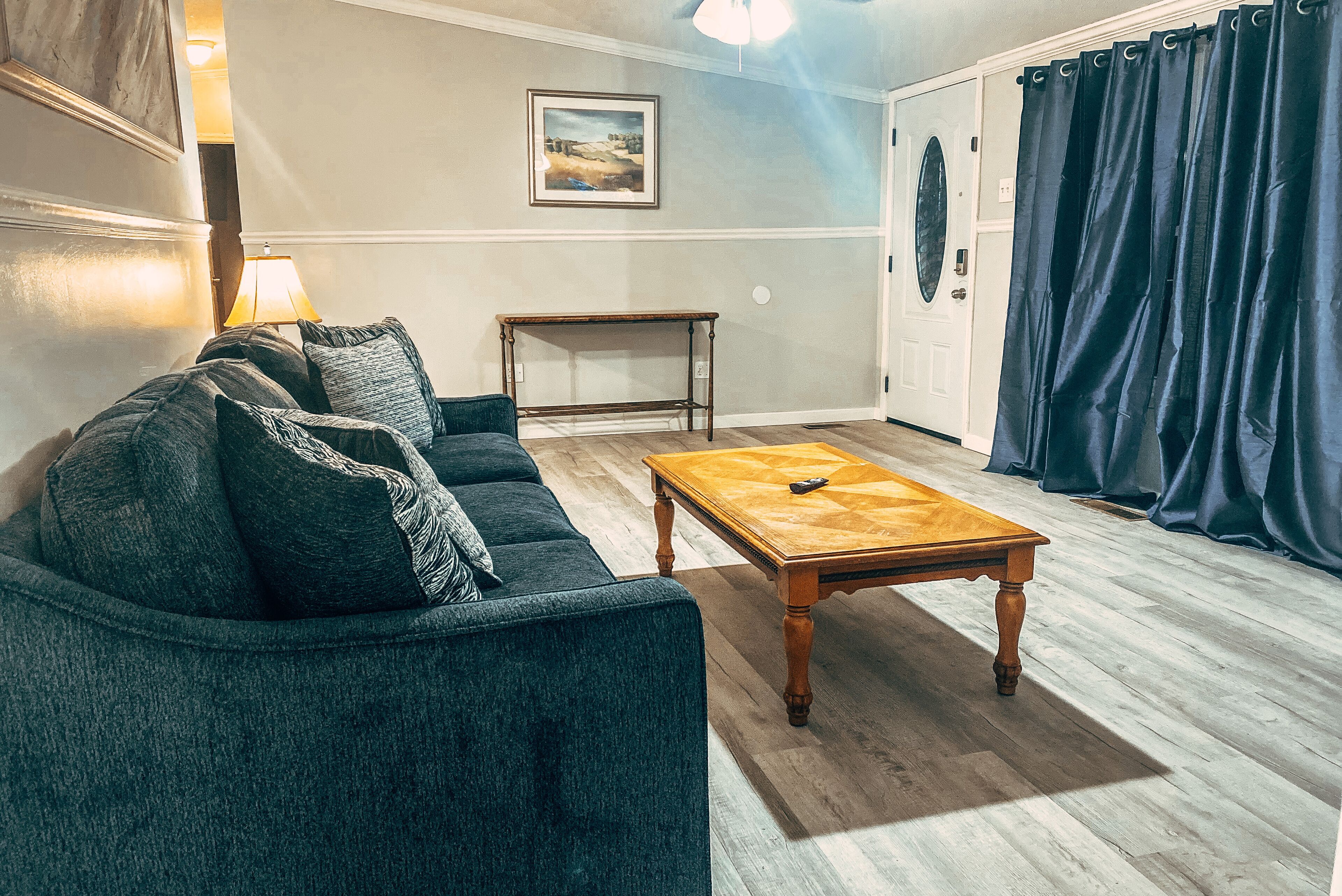 Un salon avec un canapé bleu foncé, une table basse en bois et une lampe.