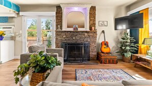 Un salon avec une cheminée, un canapé, une table basse, une guitare et un téléviseur.