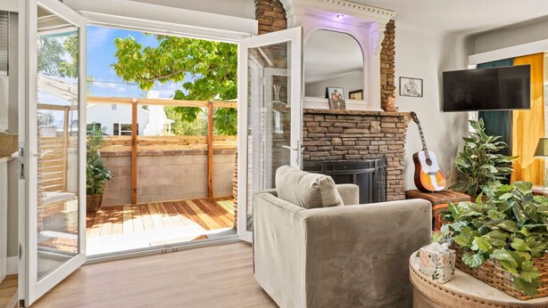 Un salon chaleureux avec une cheminée, un canapé confortable, une guitare et une grande fenêtre donnant sur un jardin.
