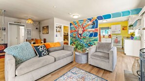 Un salon moderne avec un canapé gris, deux fauteuils et un tableau abstrait aux couleurs vives accroché au mur.