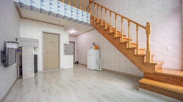 Un vaste espace de vie agrémenté d’un escalier en bois, d’un réfrigérateur blanc et d’un ventilateur de plafond.