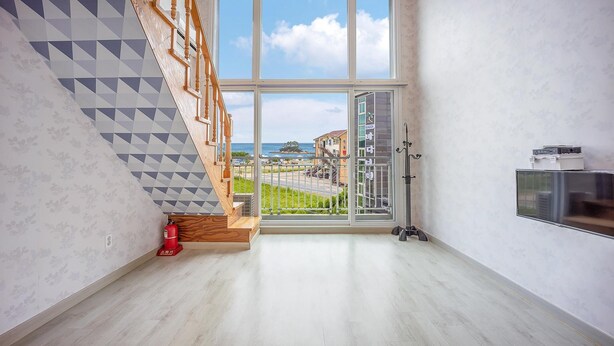 A spacious room with a wooden staircase, a large window with a view of the sea, and a fire extinguisher on the floor. - Taean Happyzonepension (Taean)