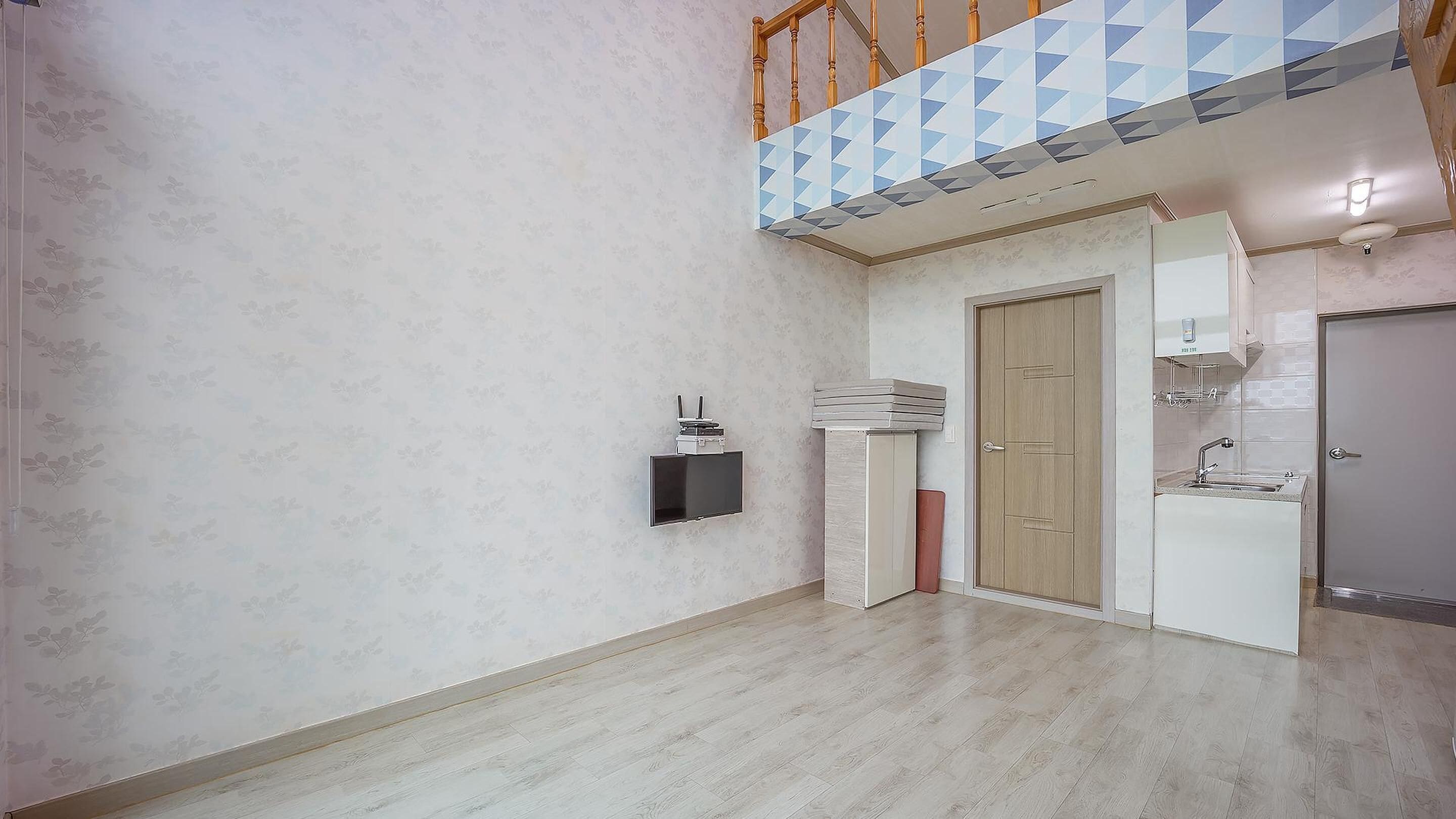 Une pièce dotée d’un plancher en bois, d’un téléviseur encastré, d’une porte et d’un coin cuisine.