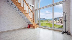 A spacious room with a wooden staircase, large windows, and a view of a coastal area. - Taean Happyzonepension (Taean)