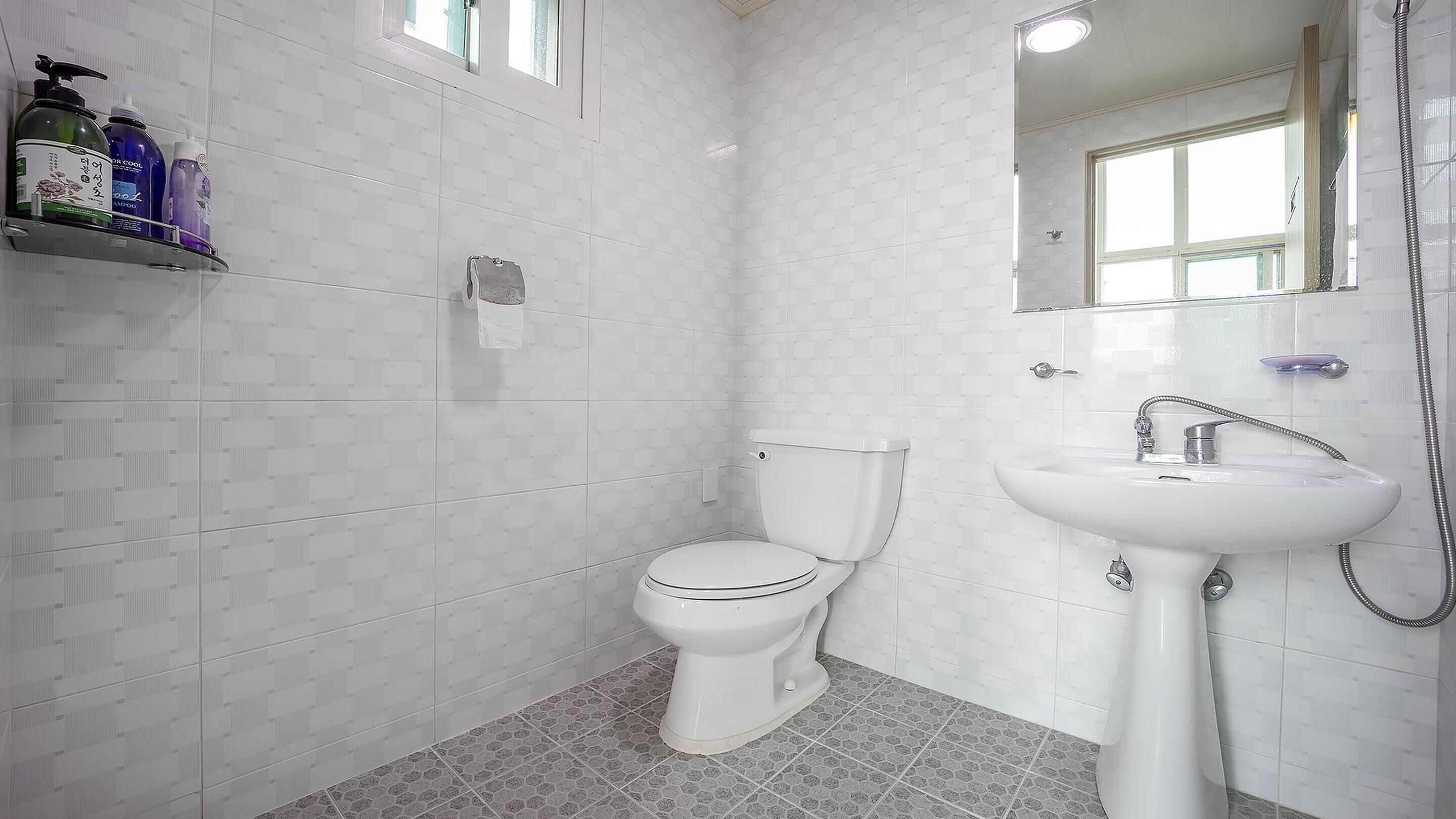 A bathroom with a toilet, a sink, and a shower. There are toiletries on a shelf.