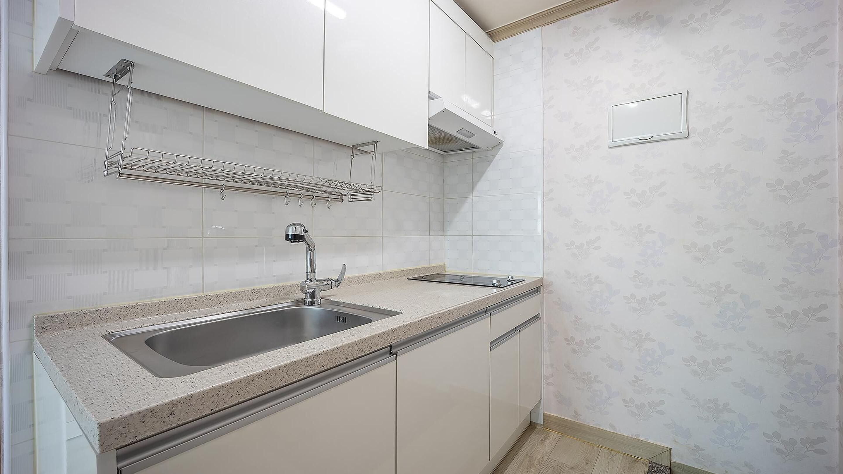 A kitchen with a stainless steel sink, white cabinets, a backsplash, and a patterned wall.