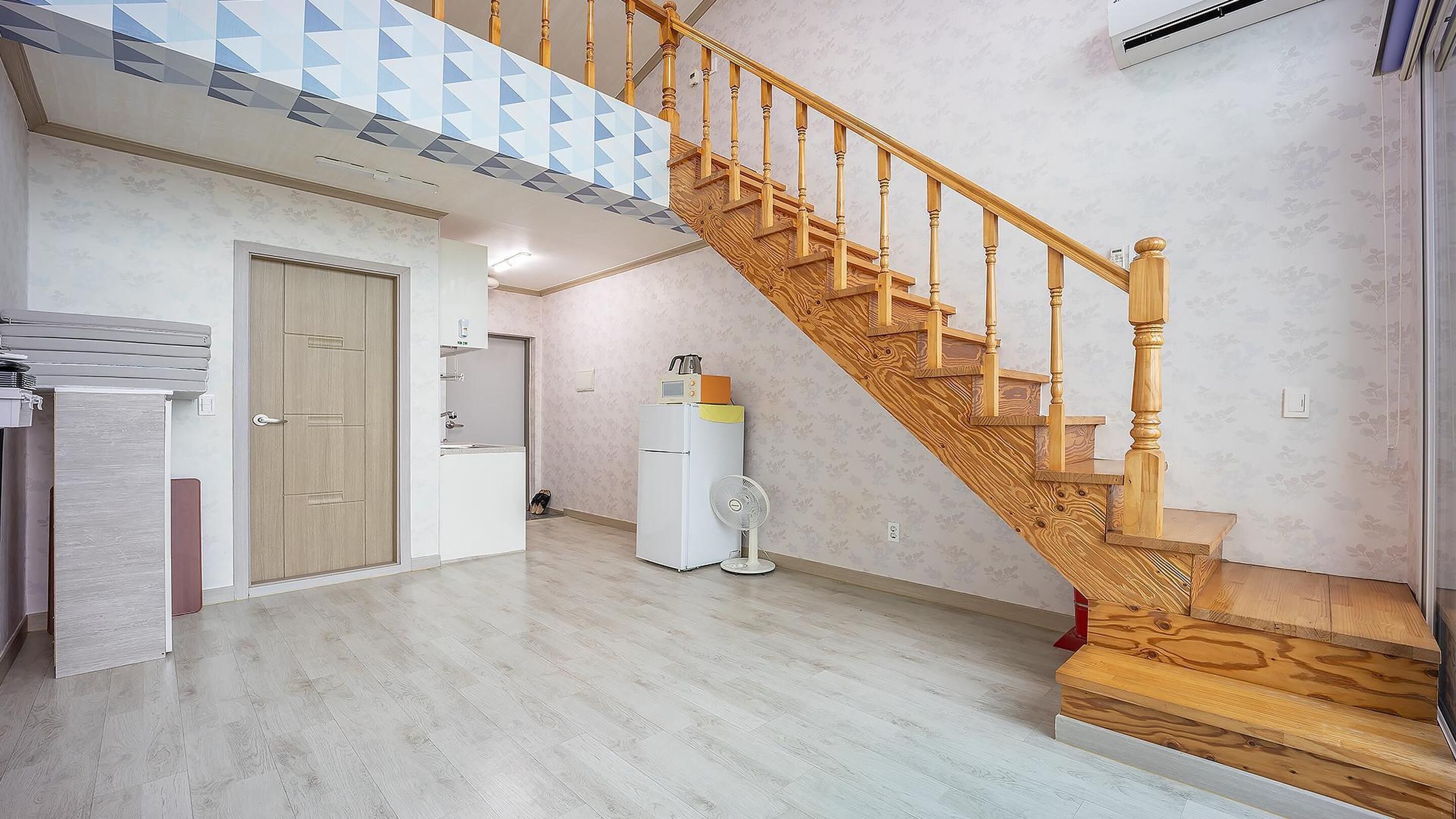A spacious living area with a wooden staircase, a kitchen area, and a white refrigerator.