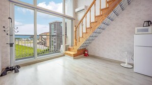 A spacious room with a large sliding glass door leading to a balcony, a wooden staircase, a white refrigerator, and a standing fan. - Taean Happyzonepension (Taean)