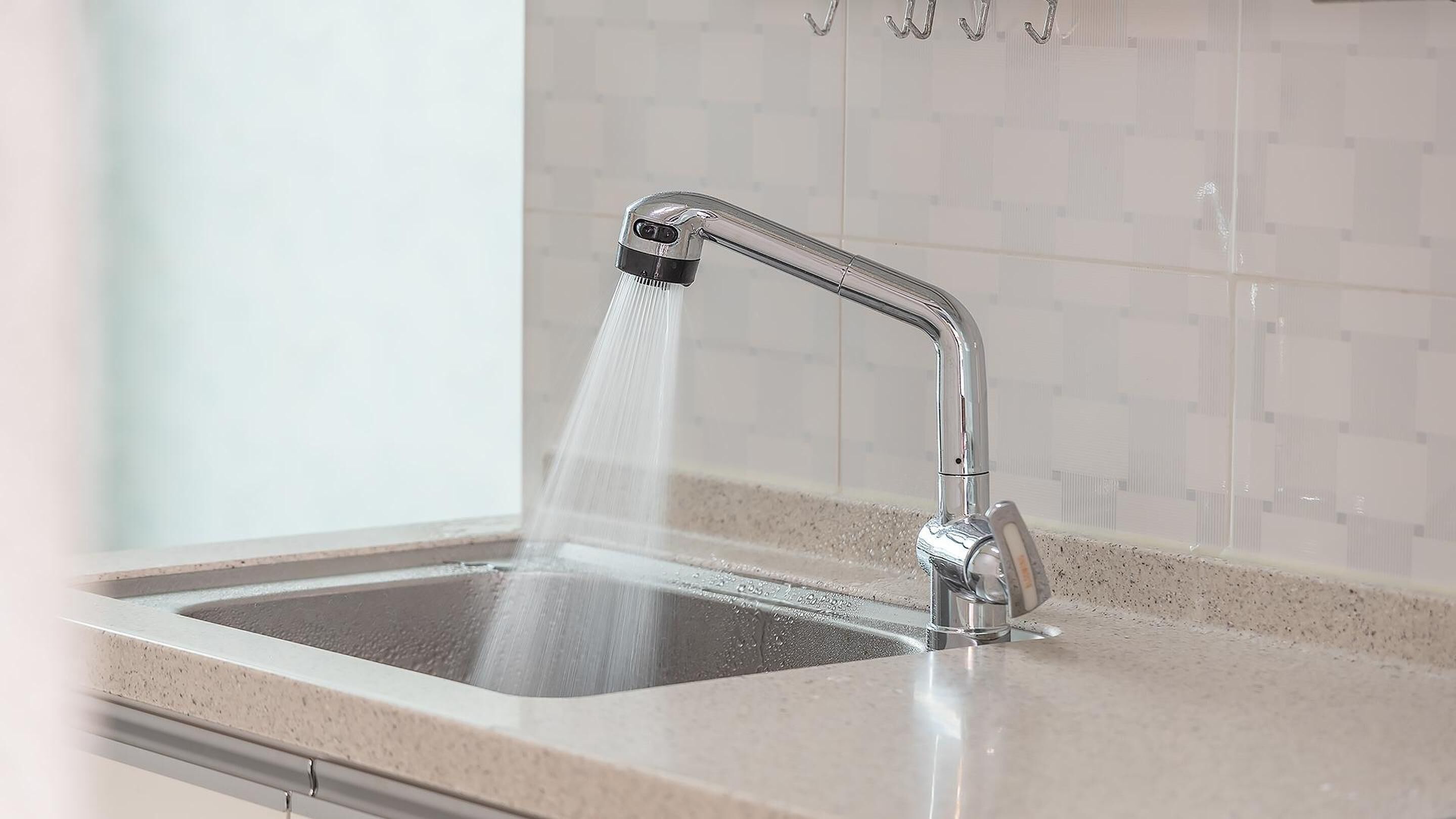 Een keukenkraan met een moderne douche en een betegelde spatwand.