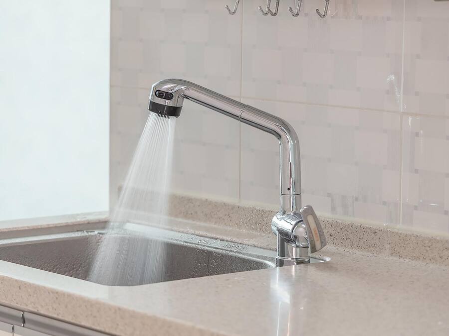 Een keukenkraan met een moderne douche en een betegelde spatwand.