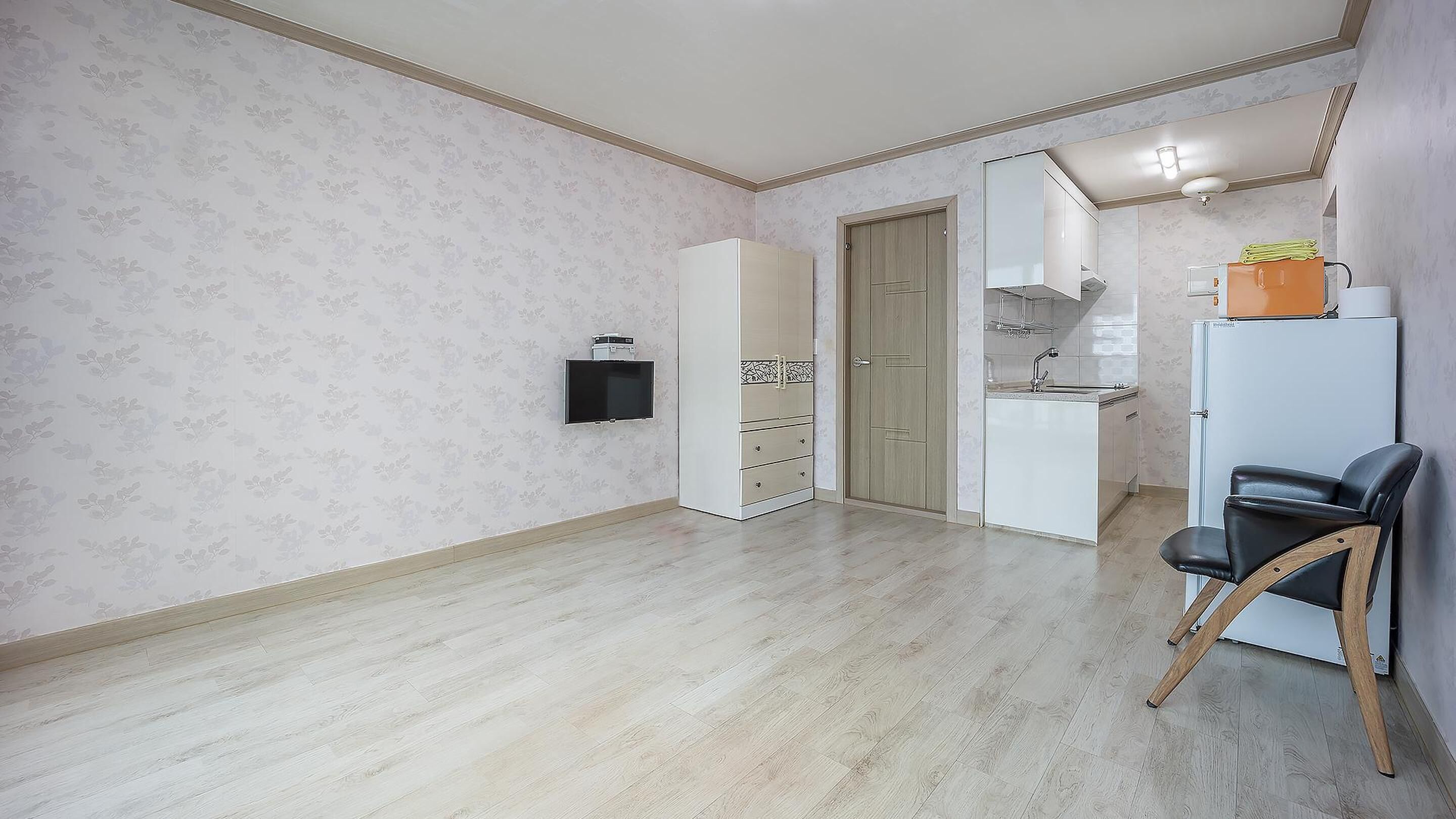 A small, open-plan living space with a kitchen area, a dining table, and a black chair.