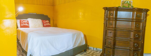 A bed with white bedding and two pillows, a wooden dresser with multiple drawers, and a yellow wall.