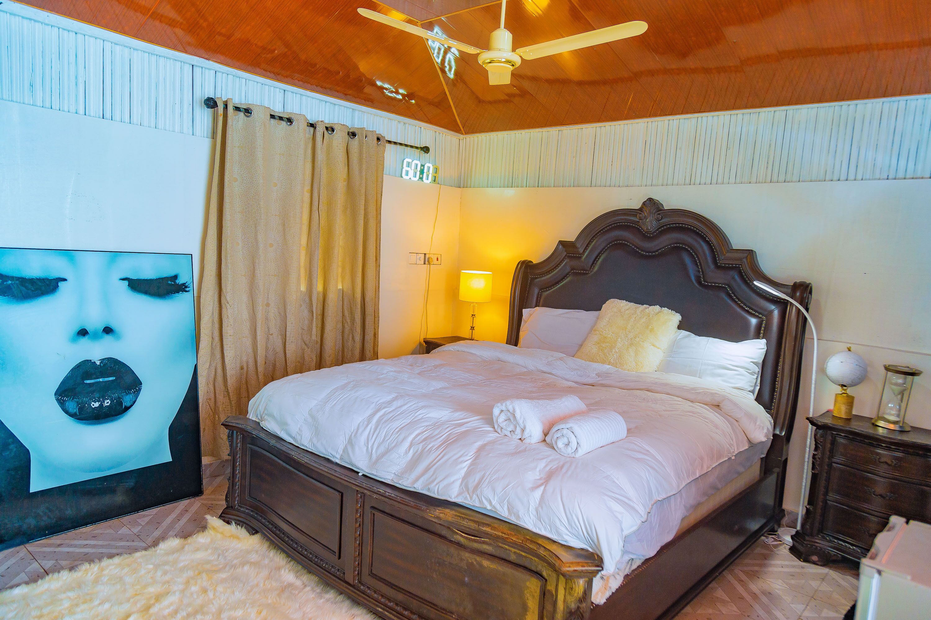 Una cama bien hecha con sábanas blancas, cabecera de madera y una lámpara de noche.
