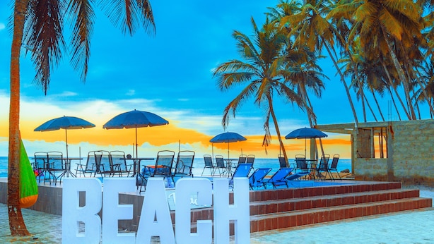 Une scène de plage avec le mot « PLAGE » écrit en grandes lettres, des palmiers et des chaises longues.