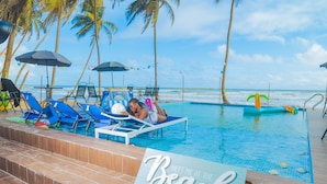 Un espace aménagé au bord de la piscine, avec des chaises longues, des parasols et un panneau indiquant : « Rendez-vous à la plage ».