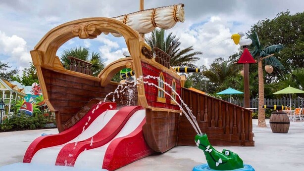 A pirate-themed water play area with a ship structure, a slide, and a green alligator figure.
