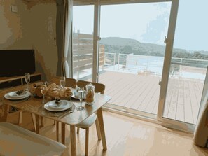 Un coin repas avec une table dressée pour deux personnes, un téléviseur et une vue sur la terrasse et les montagnes.