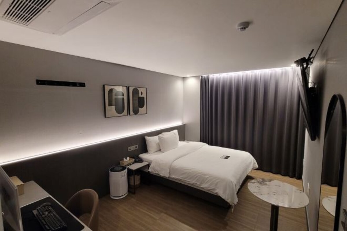 A modern hotel room with a bed, desk, chair, and a small table.