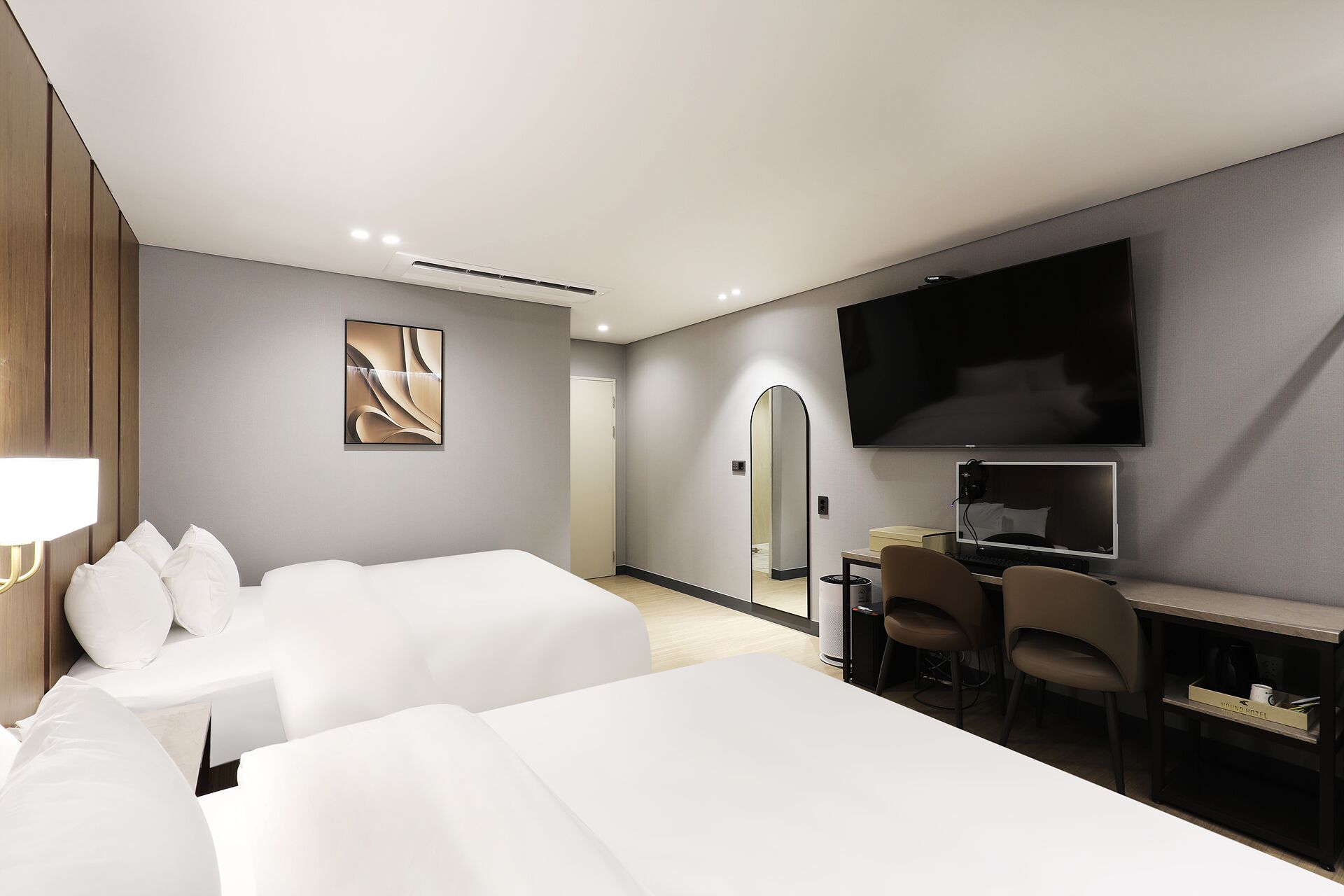 Een hotelkamer met twee bedden, een bureau met een computer, een televisie en een spiegel.