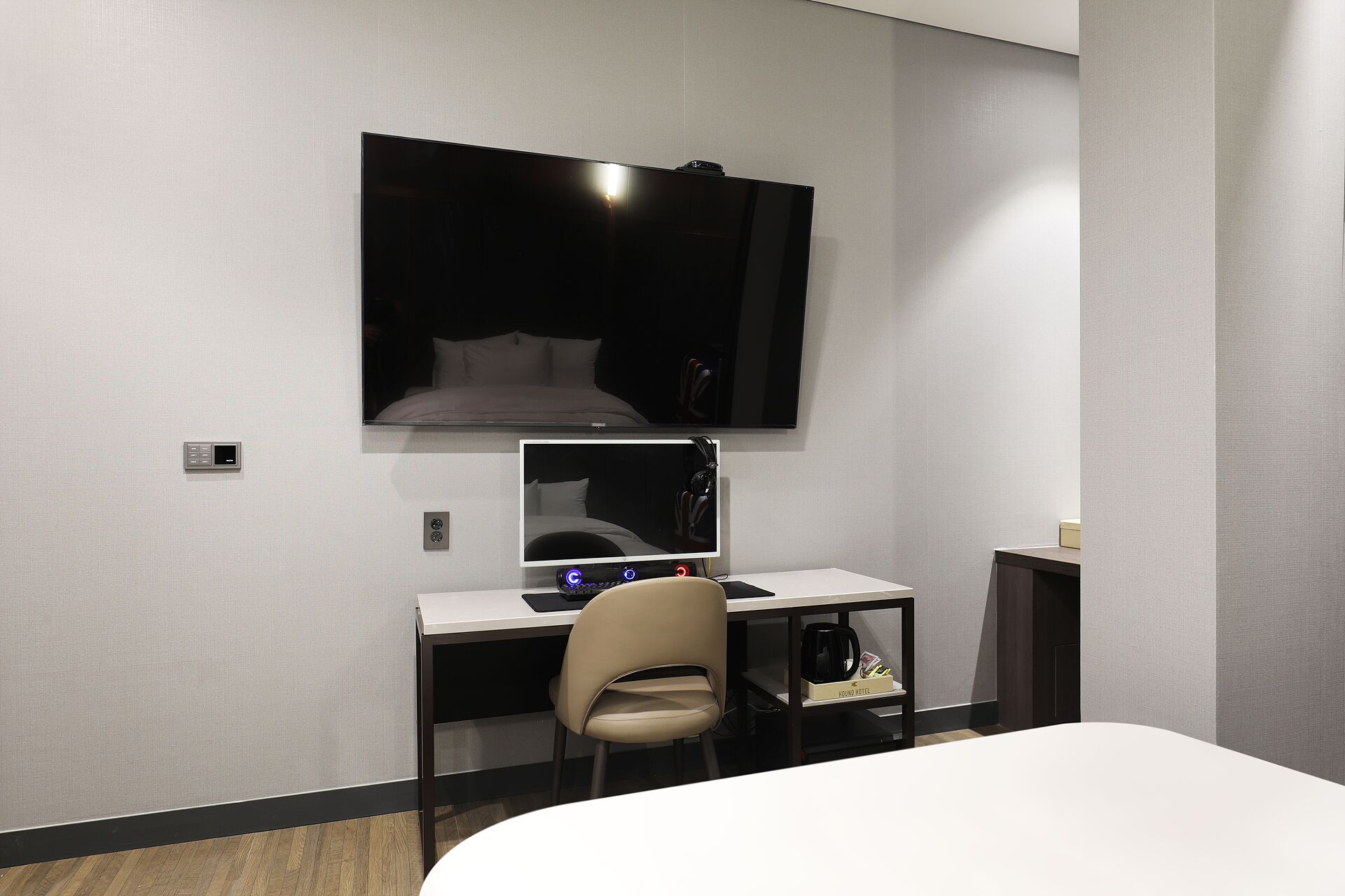 A hotel room with a bed, a desk with a computer, a chair, and a TV mounted on the wall.