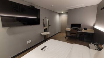 Een hotelkamer met een bed, een bureau met een computer, een televisie, een spiegel en een tafeltje.