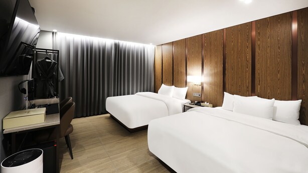 Moderni hotellihuone, jossa on kaksi sänkyä, työpöytä, tuoli, televisio ja vaatekaappi.