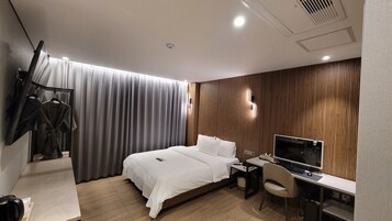 Une chambre d’hôtel moderne équipée d’un lit, d’un bureau, d’une chaise, d’une télévision et d’un miroir.