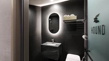 Ein modernes Badezimmer mit schwarzem Marmor, einem runden Spiegel, einem Waschbecken und einer Toilette. Ein Handtuchhalter mit dem Schriftzug "HOUND HOTEL".