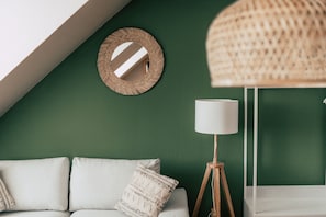A room with a green wall, a white sofa with cushions, a round mirror, and a floor lamp.