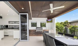 A modern kitchen with a glass door, a dining area with a glass table, and a ceiling fan. - Sandy View - 180 degree views - Luxury Home (Nikenbah)