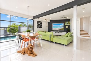 A modern living room with a pool view, a dining area, and a staircase. - Sandy View - 180 degree views - Luxury Home (Nikenbah)