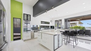 A modern kitchen with a large island, white cabinetry, and a green accent wall. - Sandy View - 180 degree views - Luxury Home (Nikenbah)