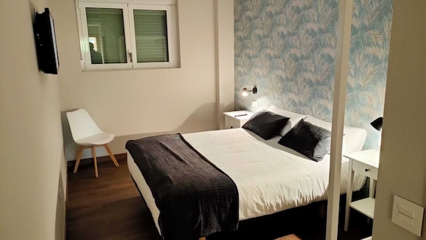 Een slaapkamer met een bed, een stoel, een nachtkastje en een raam.