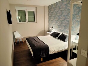 A bedroom with a bed, a chair, a nightstand, and a window.