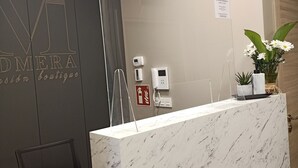 Een receptiebalie met een marmeren blad, een zwarte bureaustoel, een beveiligingscamera, een brandblusser en een plant.