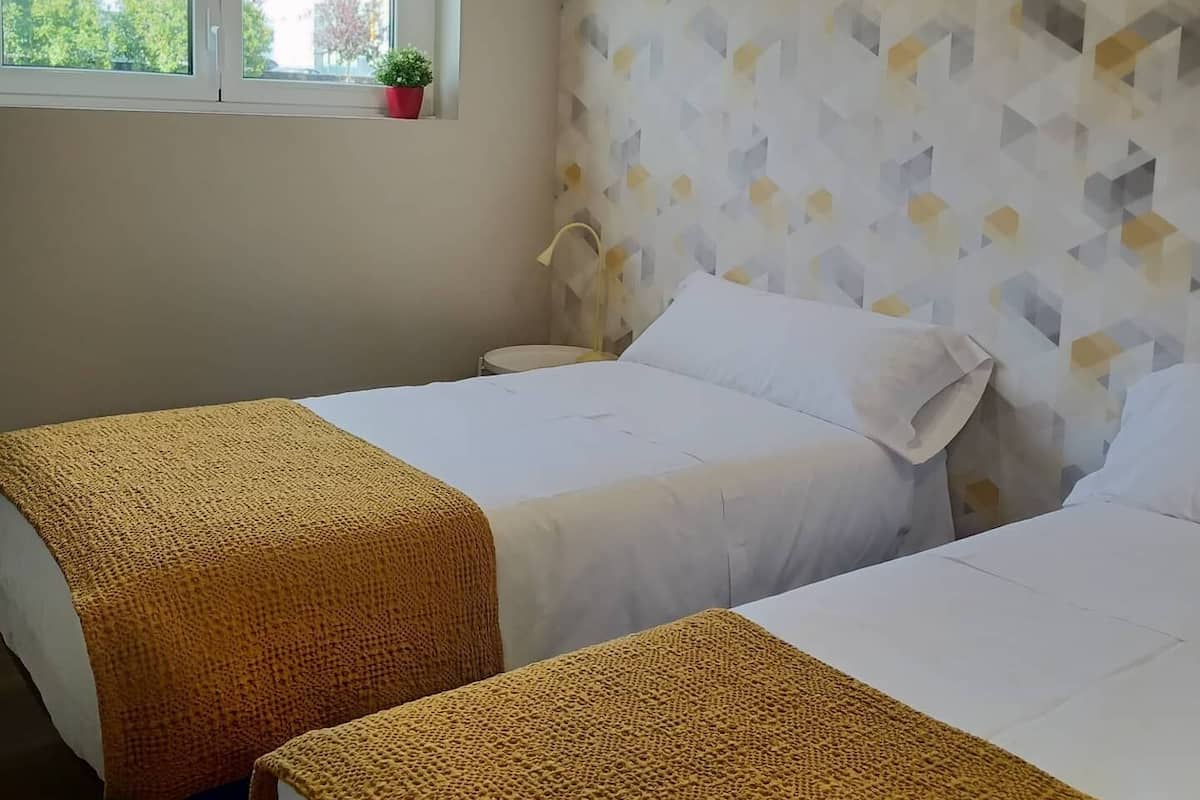 Habitación de hotel con dos camas, una ventana que da a zonas verdes y una pared con diseño geométrico.