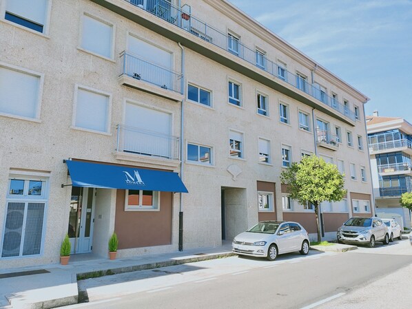 A multi-story building with a blue awning, a car parked in front, and a tree on the sidewalk.