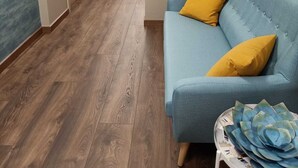 Een hal met houten vloeren, een blauwe bank met gele kussens, en een kunstwerk aan de muur van een hoed.