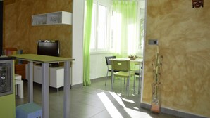 A compact living space with a dining area, a television, and a window with green curtains. - Beautiful oasis with pool landscape near the dream beach Las Marinas (Dénia)