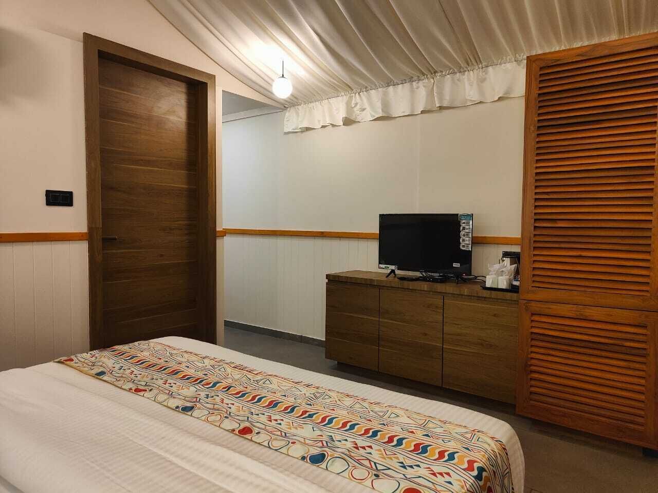 Une chambre d’hôtel avec un lit, une armoire en bois, une télévision et un rideau.