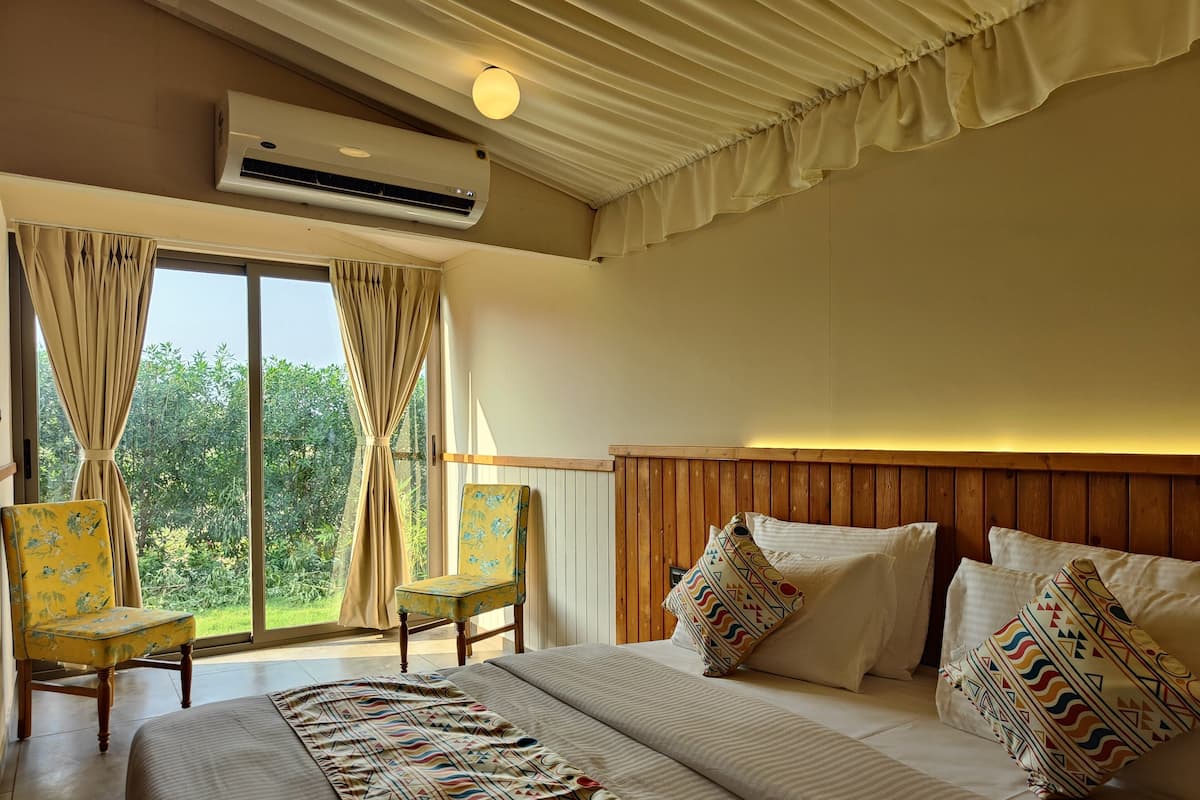 A hotel room with a large bed, a wooden headboard, and a view of greenery through the window.