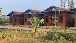 A row of wooden buildings with a flat roof and a small garden area in front. - Nirvana Resort and Restaurant (Garudeshwar)