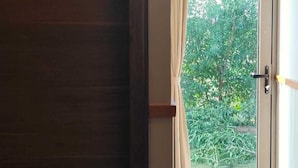 A room with a sliding glass door leading to a balcony with a view of greenery. - Nirvana Resort and Restaurant (Garudeshwar)