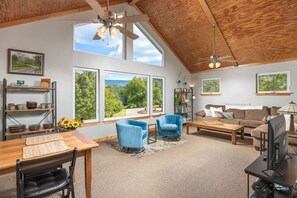 Relax in this spacious living room with a high ceiling and large windows offering a view of the surrounding landscape.