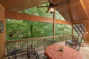 Relax on the deck with a ceiling fan above, surrounded by a lush forest view.