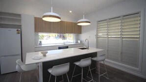 Cozinha moderna com ilha central, banquetas brancas, iluminação pendente e vista para o exterior através de uma janela.