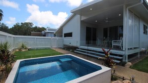 Uma casa moderna com piscina, alpendre coberto e quintal cercado.