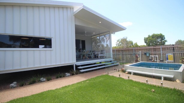 Uma casa moderna com varanda coberta, piscina e gramado bem cuidado.